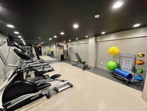 Een sportschool met fitnessapparatuur, waaronder loopbanden en hometrainers, en een wandrek met fitnessballen.