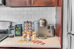 A kitchen counter with a coffee maker, a kettle, a coffee grinder, a bag of coffee beans, and various coffee pods. - 20 MIN to Manhattan! 2BR Luxurious Comfy & Spotless (Newark)