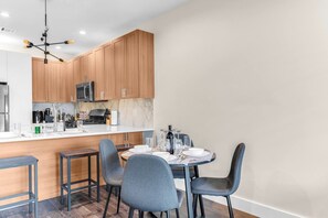 A modern kitchen with wooden cabinets, a central island, and a dining area with grey chairs. - Lux! Gym! King bed-Free Parking Long Term Friendly (Plainfield)