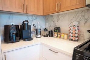 A kitchen with a coffee maker, blender, kettle, and a spice rack. - Lux! Gym! King bed-Free Parking Long Term Friendly (Plainfield)