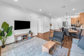 Ein modernes Wohnzimmer mit Fernseher, Couch, Esstisch und Stühlen.