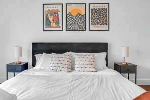 Une chambre à coucher avec un lit, deux tables de chevet et trois œuvres d’art encadrées accrochées au mur.