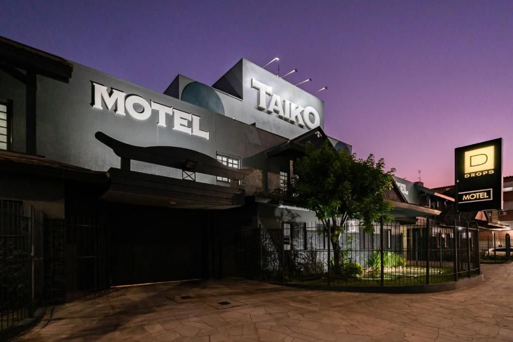 Un motel con un letrero llamativo que dice 'TAIKO MOTEL' y un letrero más pequeño que indica 'DROPS MOTEL' al fondo.
