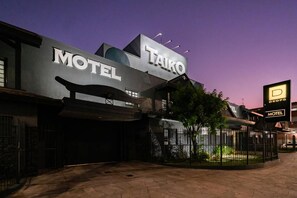 Un motel con un letrero llamativo que dice 'TAIKO MOTEL' y un letrero más pequeño que indica 'DROPS MOTEL' al fondo.