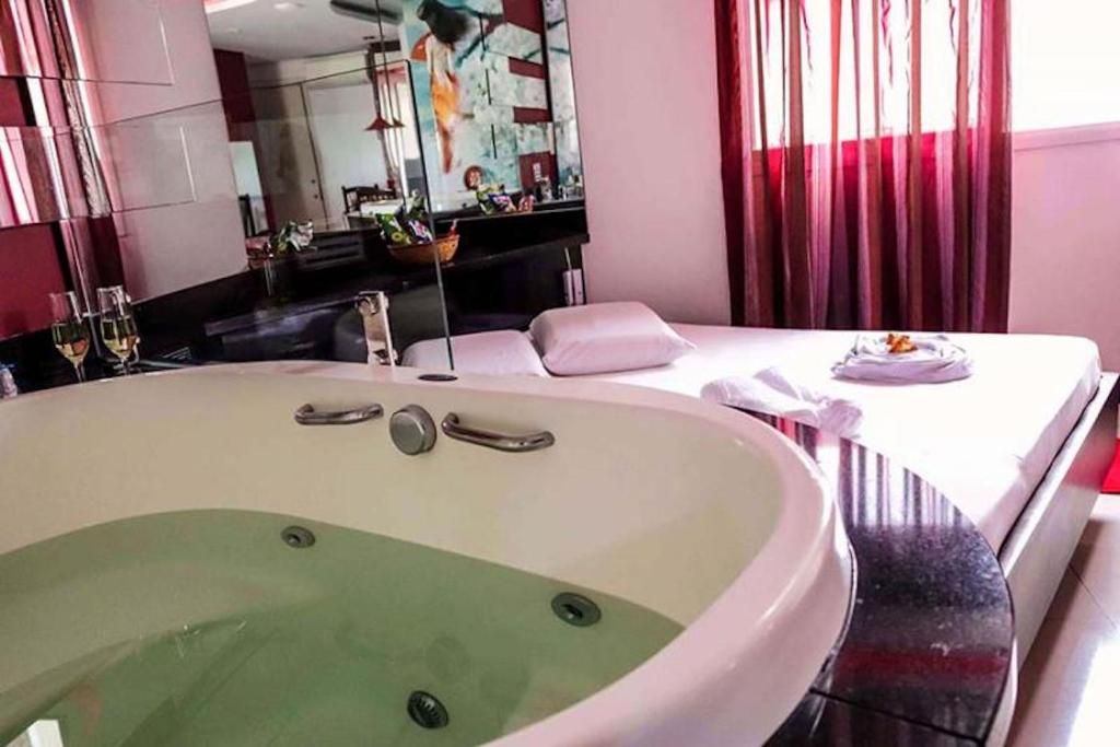 A hotel room with a large bathtub, a bed with a white comforter, and a dining table set with a plate and a glass.