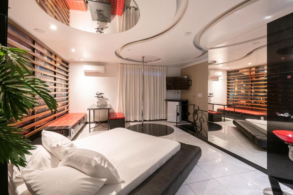 Habitación de hotel moderna con una cama, un escritorio, una silla, un televisor y un baño con un lavamanos rojo.