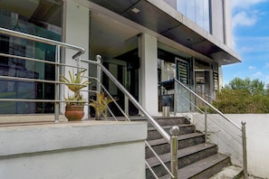 Entrada de um edifício com escadas, plantas em vasos e guarda-corrimão de metal.