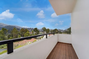 Varanda com piso de madeira e guarda-corpo preto, com vista para área residencial com árvores e casas sob um céu claro.