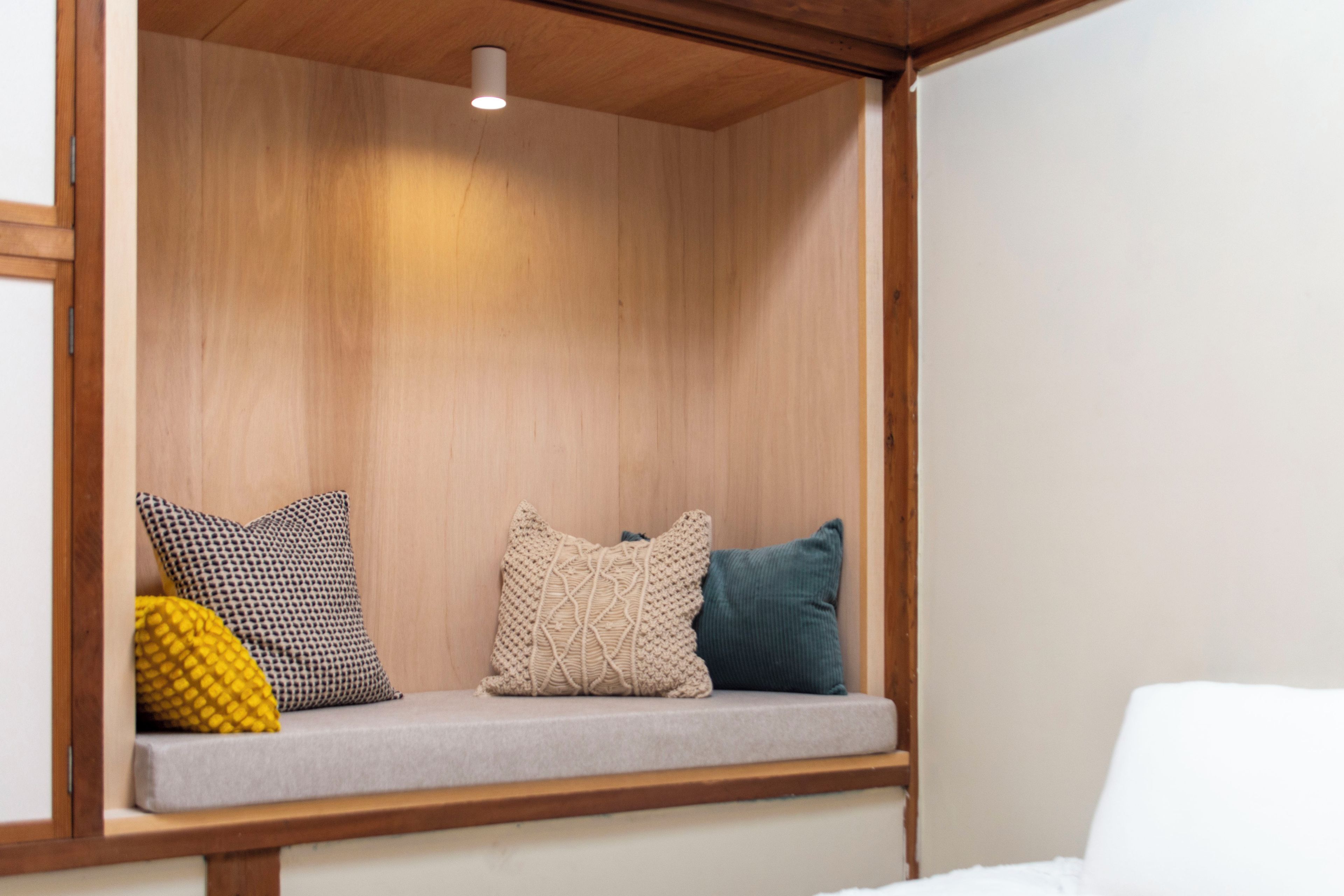 A wooden bench with cushions, a ceiling light, and a white wall.