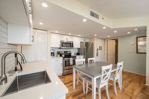 A modern kitchen with stainless steel appliances, a dining area with white chairs, and a wooden floor. - RUM CAY AT SUNRISE SUITES - 2 Bedroom / 2 Bathroom w/ Shared Pool, Spa, Parking (Key West)