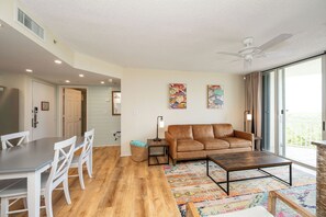 A living room with a brown leather sofa, a coffee table, a dining table with chairs, and a colorful rug. - RUM CAY AT SUNRISE SUITES - 2 Bedroom / 2 Bathroom w/ Shared Pool, Spa, Parking (Key West)