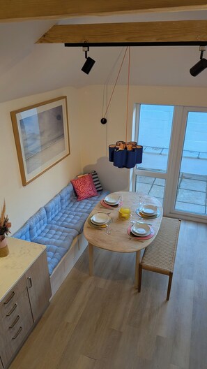 Ein modernes Wohnzimmer mit Essbereich, einer blauen gepolsterten Bank, einem runden Tisch für vier Personen und einem großen Fenster mit Blick.