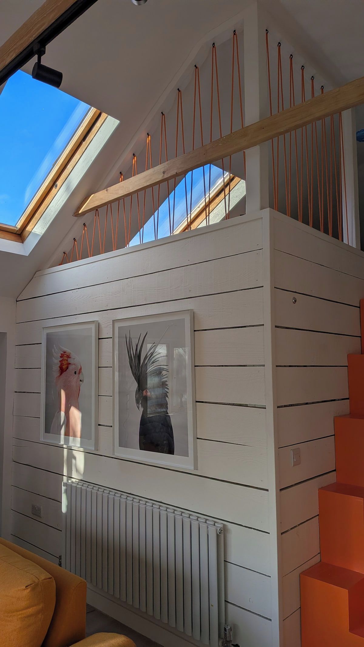 A modern interior with a skylight, white wooden paneling, a radiator, and orange steps.