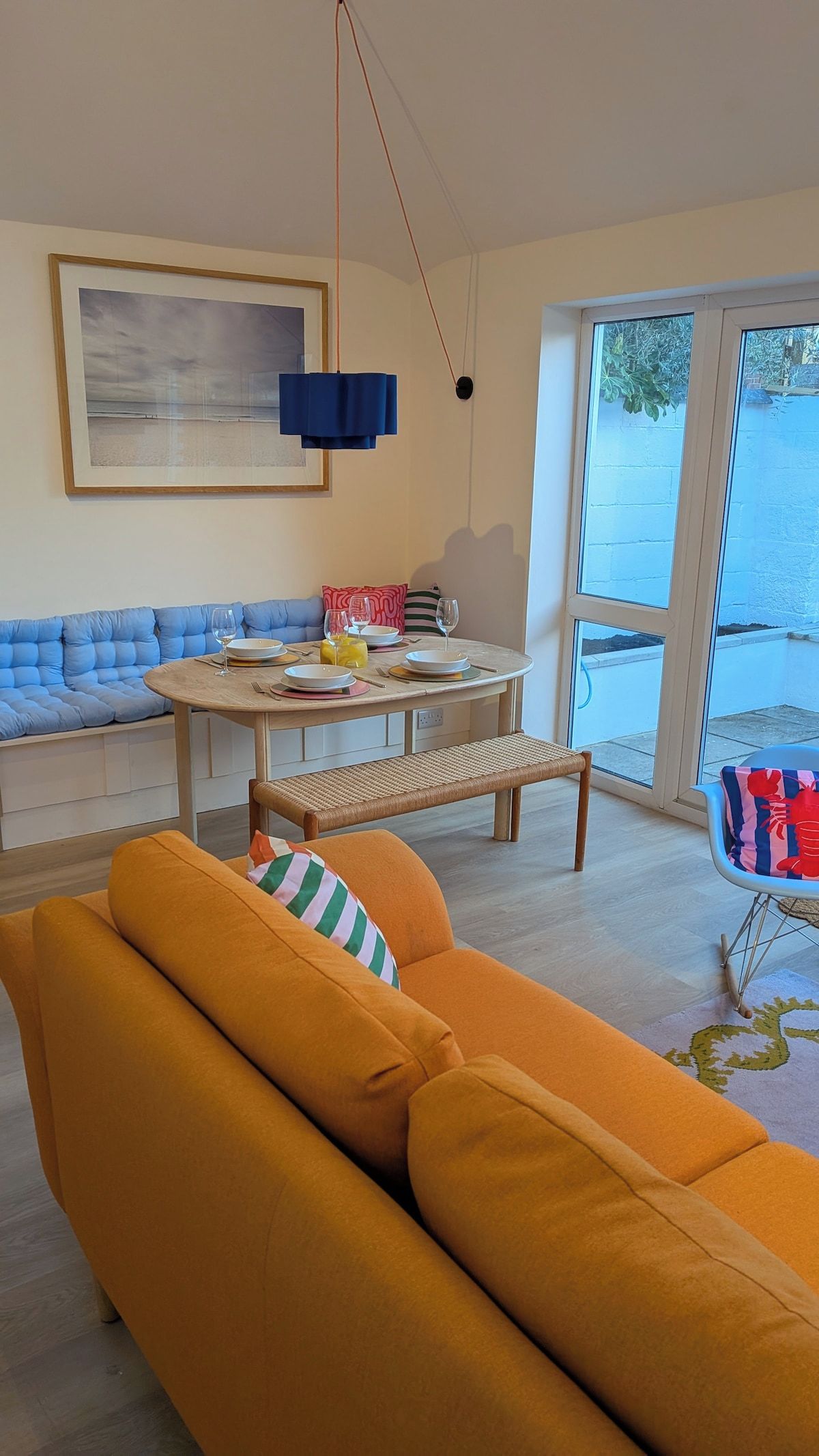 A modern living room with a sofa, a dining table with chairs, a bench, and a large window.
