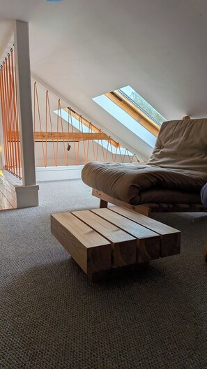 Ein Schlafzimmer im Loft-Stil mit schrägem Dach, einer Holzbank, einer gepolsterten Bank, einer Hängematte und einem Dachfenster.