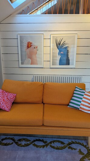 Ein Zimmer mit einer Couch, zwei Kissen, einem Heizkörper und zwei gerahmten Kunstwerken an der Wand.