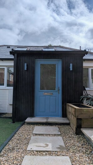 Una piccola costruzione in legno con una porta blu, una finestra e una maniglia metallica.