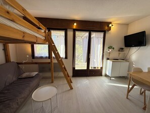 Quarto com cama de solteiro, sofá, mesa pequena, escrivaninha e televisão presa na parede.