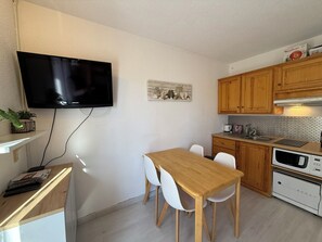 Cozinha compacta com armários de madeira, micro-ondas, TV Samsung e mesa de jantar com cadeiras.