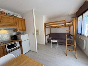 A compact room with a kitchenette, bunk beds, and a small table. - Studio 4pers - terrasse - 300m des pistes (Guillaumes)