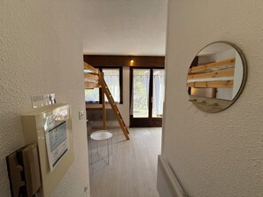 Quarto com cama beliche, escada, mesa pequena e espelho na parede.