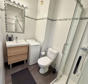 Un baño moderno con cabina de ducha de vidrio, inodoro blanco, tocador con espejo y una pequeña alfombra en el suelo.