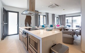A modern kitchen with an island, built-in oven, and a dining area with a table and chairs. - Luxury Penthouse with a Pool View Balcony at Brand New Walishali Condos (Oranjestad)