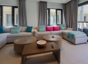 A modern living room with a sectional sofa, two coffee tables, and a remote control on one of the tables. - Luxury Penthouse with a Pool View Balcony at Brand New Walishali Condos (Oranjestad)