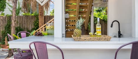 A bar area with a white countertop, purple chairs, a bottle of Sun Pop Lemonade, a pineapple, and a large glass pitcher.