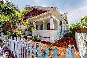 Una casa a un piano con veranda, una recinzione in legno bianco e un’aiuola con pacciamatura rossa.