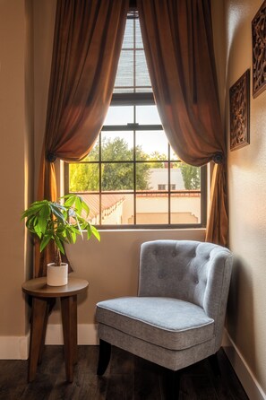 A corner room with a window, a chair, a small table with a potted plant, and a wall-mounted picture. - Boutique Hotel Suite for Two in the Historic Oroville Inn (Oroville)