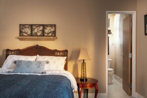 A bedroom with a wooden bed, a bedside lamp, and a wall-mounted artwork. - Boutique Hotel Suite for Two in the Historic Oroville Inn (Oroville)