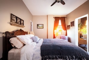 A bedroom with a bed, a ceiling fan, a window with curtains, and wall art.
