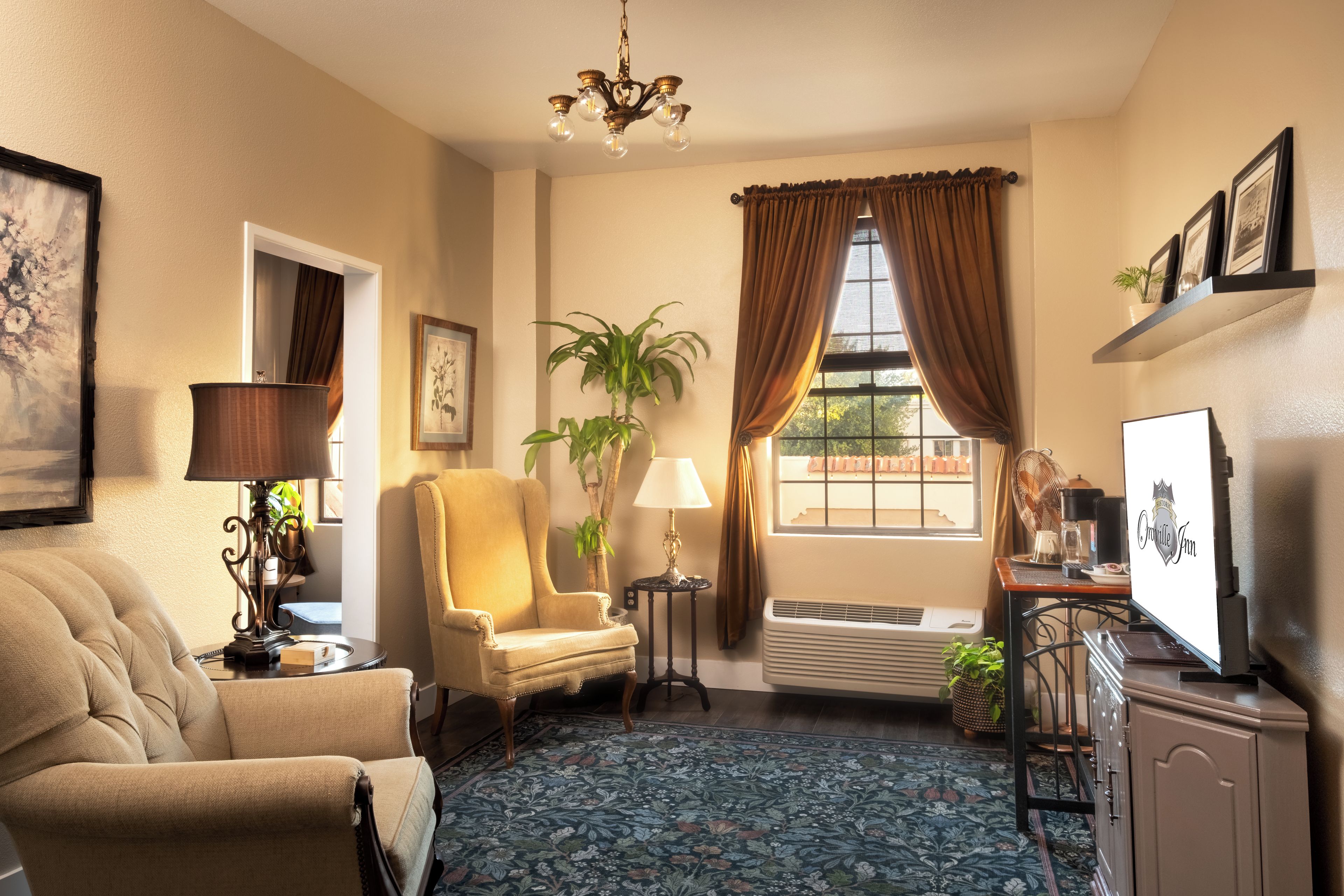 A well-lit room with a sofa, armchair, a table with a lamp, a potted plant, a radiator, and a window with curtains.