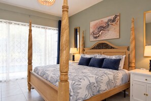 A four-poster bed with a floral bedspread, a nightstand with a lamp, a painting on the wall, and a window with curtains. - 5BR Gleenbrook Home w/ Private Pool&Spa and games (Clermont)