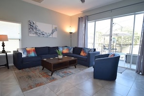 A living room with a sofa, coffee table, and a view of the outdoors. - 5BR Gleenbrook Home w/ Private Pool&Spa and games (Clermont)