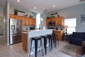 A modern kitchen with stainless steel appliances, wooden cabinets, and a central island with bar stools. - 5BR Gleenbrook Home w/ Private Pool&Spa and games (Clermont)