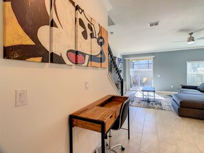 Una sala de estar con una escalera, un comedor y un cuadro abstracto grande en la pared.