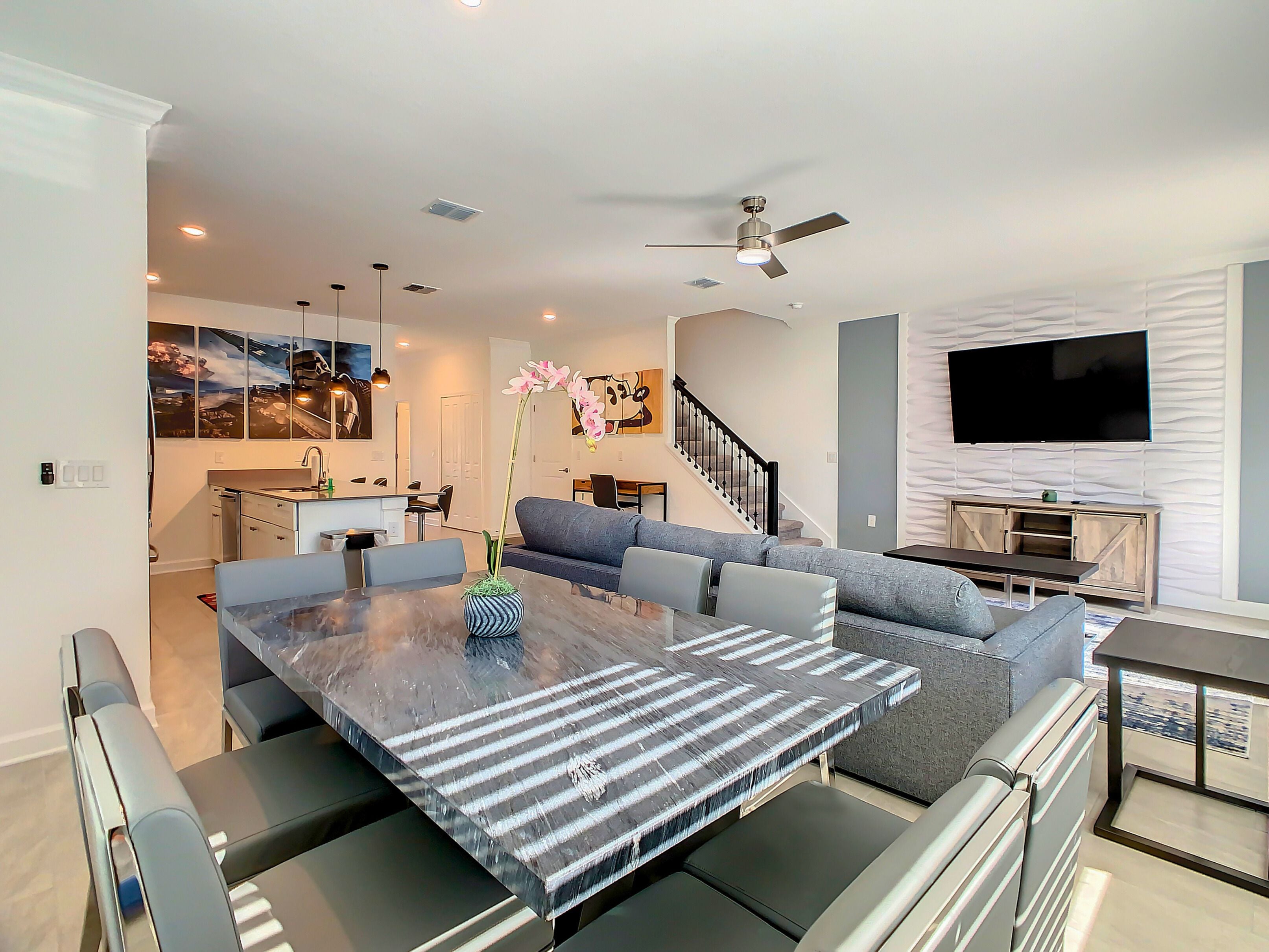 A modern living space with a dining area, sofa, TV, and a staircase.