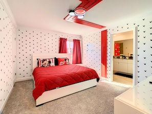A bedroom with a red bedspread, Mickey Mouse themed pillows, and a white headboard. - 5BRStorey Lake Resort | Private Pool | Near Disney (Kissimmee)
