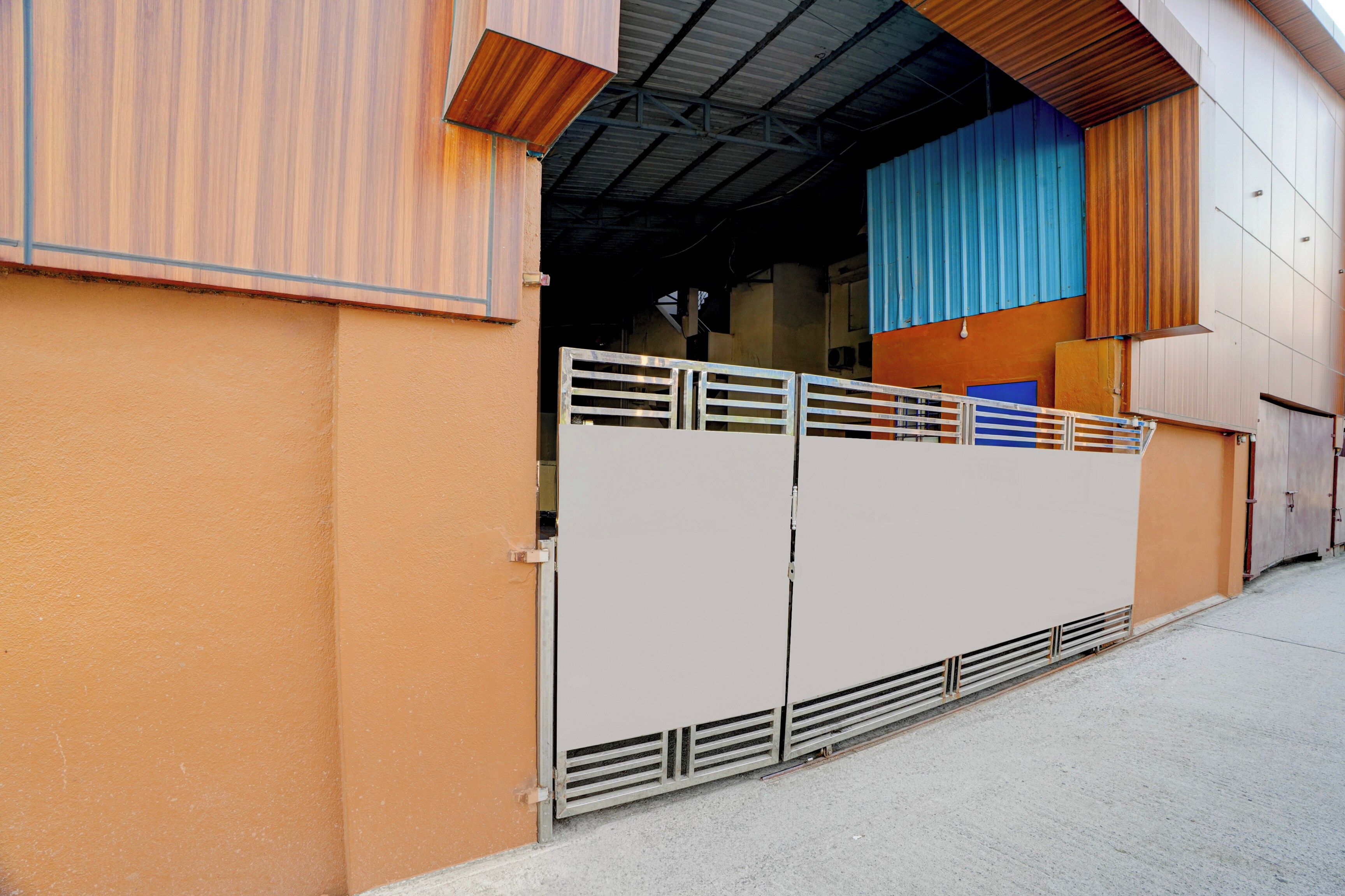 Un edificio con una verja metálica, un muro azul y naranja, y un techo de chapa corrugada.