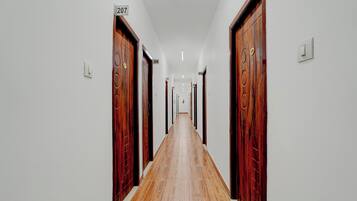 Un pasillo largo y estrecho con puertas de madera y paredes blancas, cada puerta con un número.
