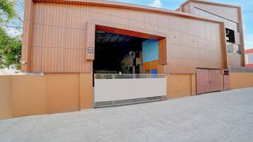 Un edificio moderno con una amplia entrada abierta, una zona cubierta con techo azul y un camino de entrada cerrado por una reja.