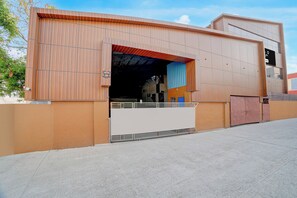 Un edificio moderno con una amplia entrada abierta, una zona cubierta con techo azul y un camino de entrada cerrado por una reja.