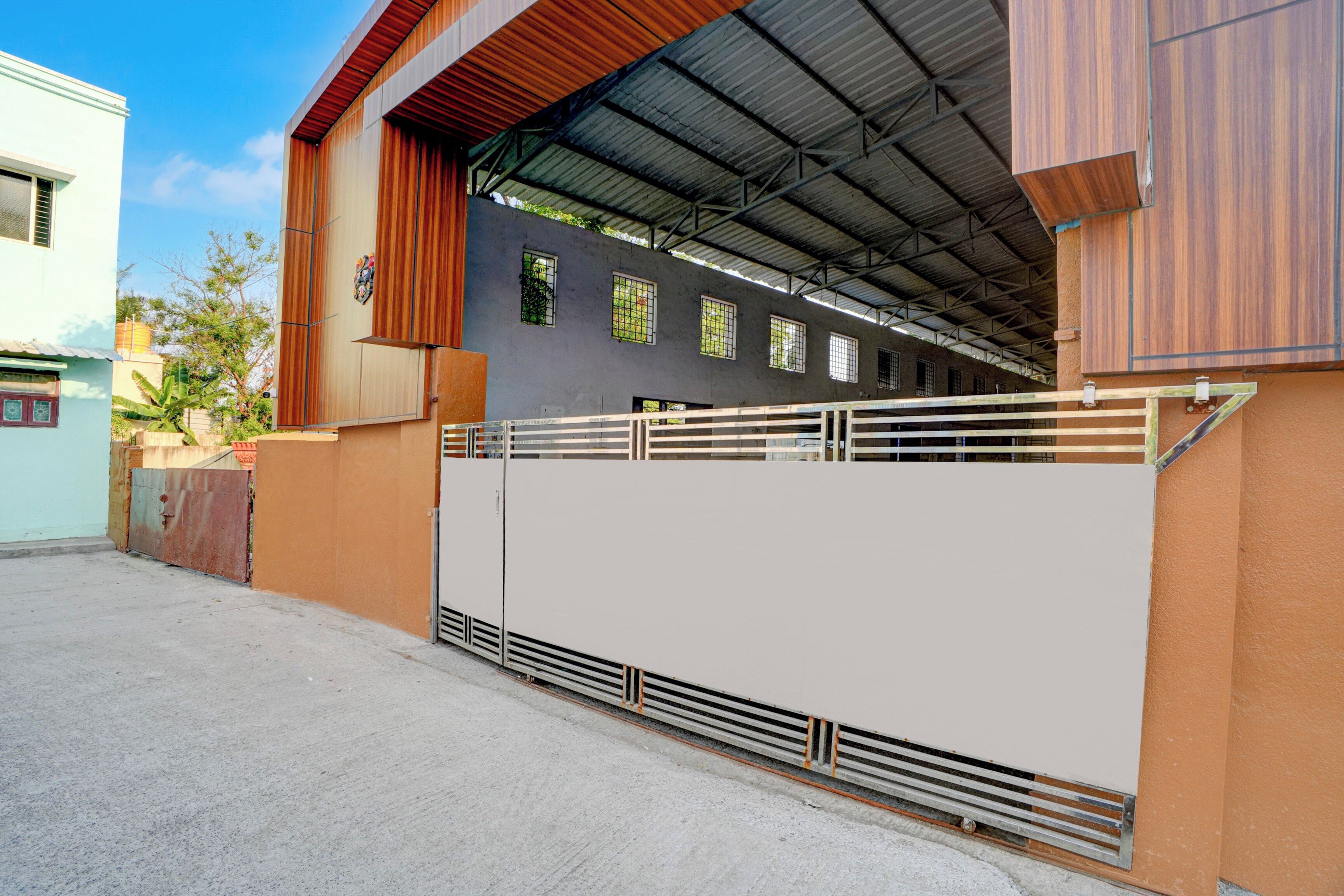 Un edificio con un gran portón metálico, una zona cubierta con techo y una pared con ventanas.