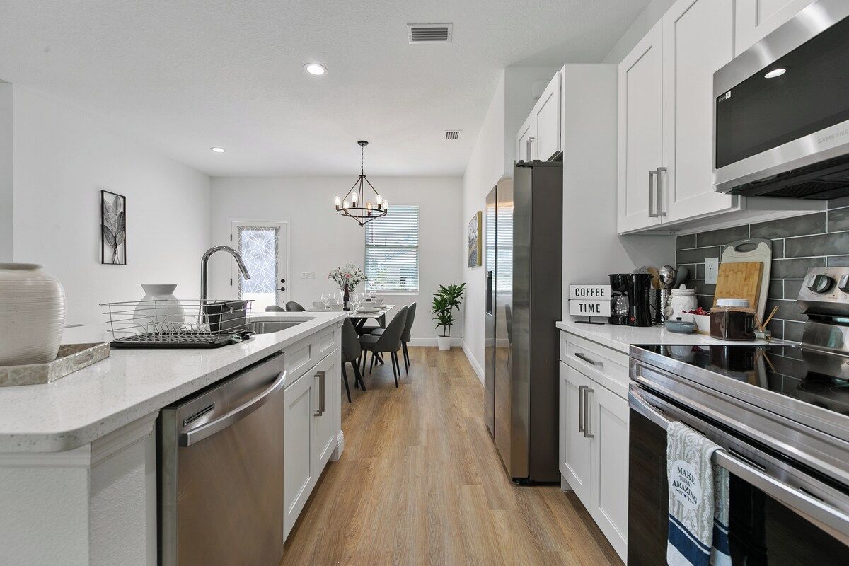 A modern kitchen with stainless steel appliances, a dining area with a chandelier, and a sign that reads 'COFFEE TIME'.