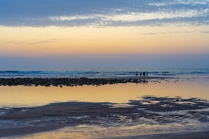 A beach scene with a calm sea, a clear sky, and a few people standing on the shore. - Sunshine Retreat | NEW 4/2, King Bed, Near Beaches (Port Charlotte)