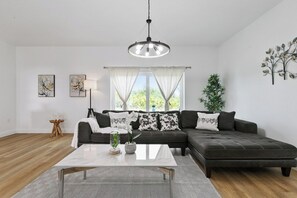 A modern living room with a sectional sofa, a coffee table, and a hanging light fixture. - Sunshine Retreat | NEW 4/2, King Bed, Near Beaches (Port Charlotte)