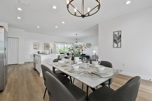 A modern kitchen with white cabinetry, a dining area with a marble table, and a chandelier. - Sunshine Retreat | NEW 4/2, King Bed, Near Beaches (Port Charlotte)