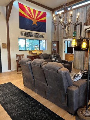 A modern living room with a sectional sofa, a large flag, a chandelier, and a rustic wall. - Inviting 3-Bedroom Sonoita Escape: The Ideal Arizona Wine Country Getaway (Sonoita)